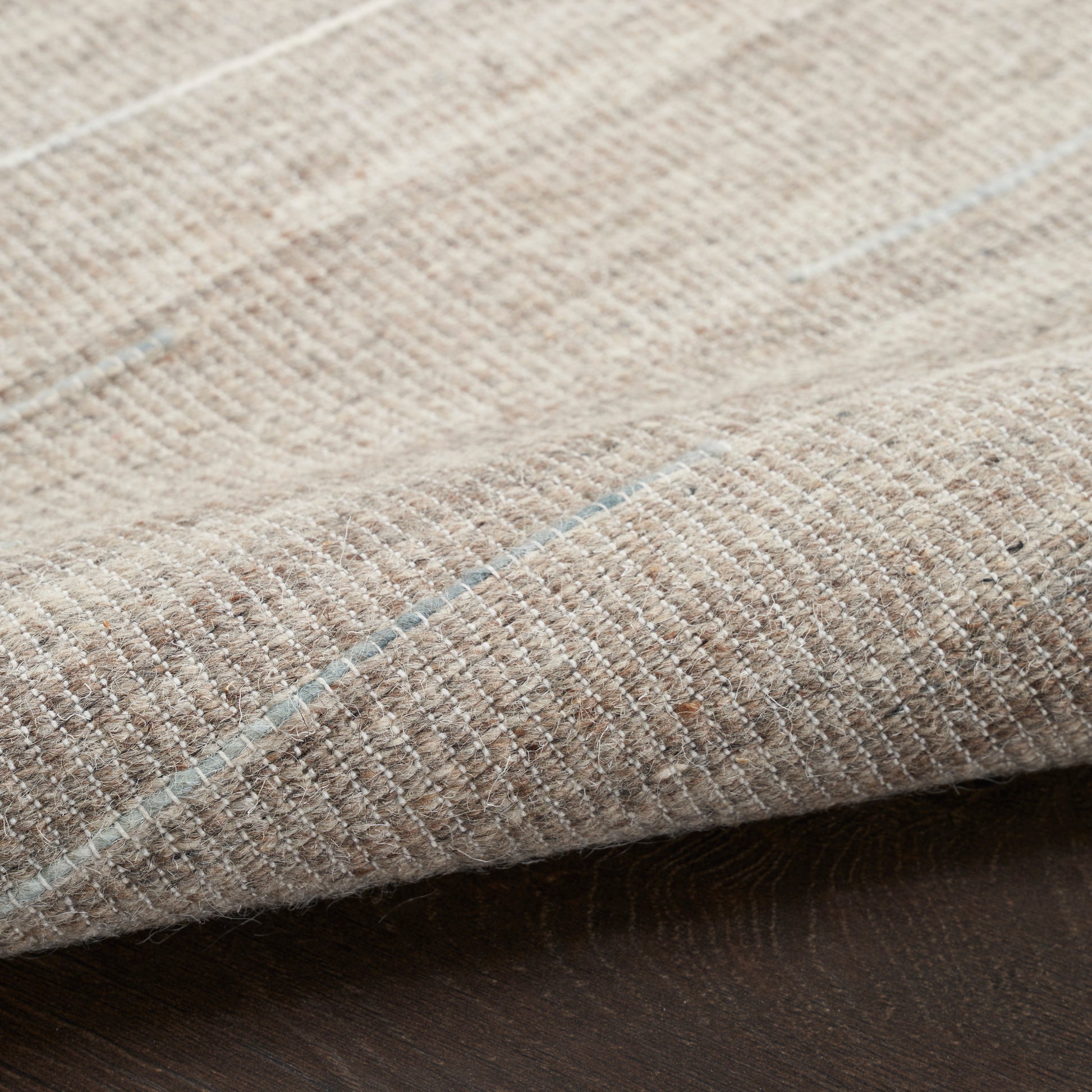 Beige woven rug with subtle light blue stripes; textured flat-weave style for neutral home decor.