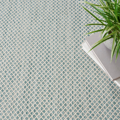 Blue & cream woven rug with diamond pattern; textured, casual home decor, shown with a plant & magazines.