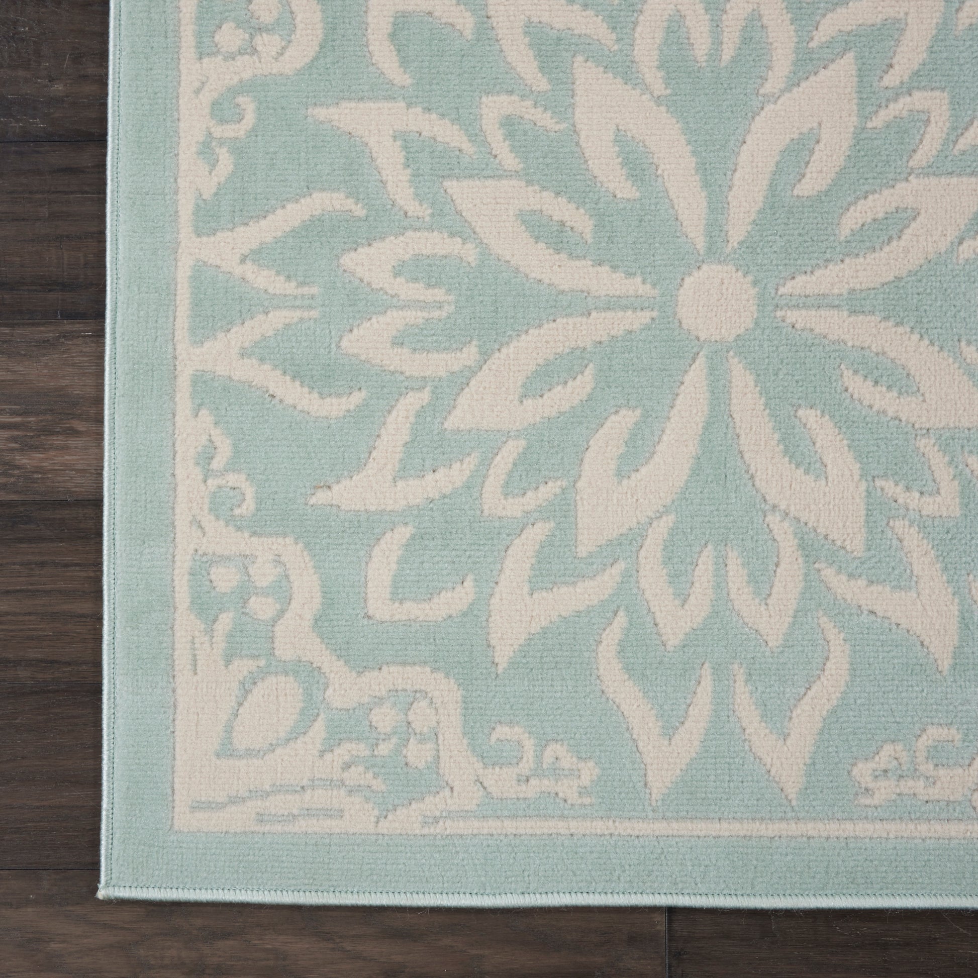 Teal and white decorative area rug with a large floral mandala pattern, woven texture, on a dark wooden floor.