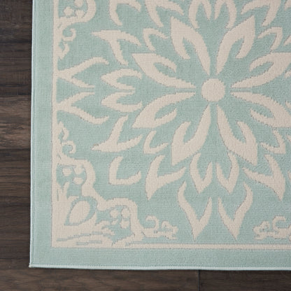 Teal and white decorative area rug with a large floral mandala pattern, woven texture, on a dark wooden floor.