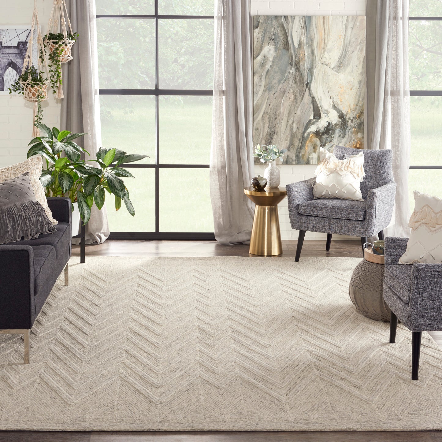 Beige chevron area rug anchors a light neutral living room with gray seating, plants, and a gold accent table.
