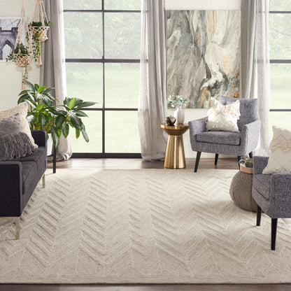 Beige chevron area rug anchors a light neutral living room with gray seating, plants, and a gold accent table.