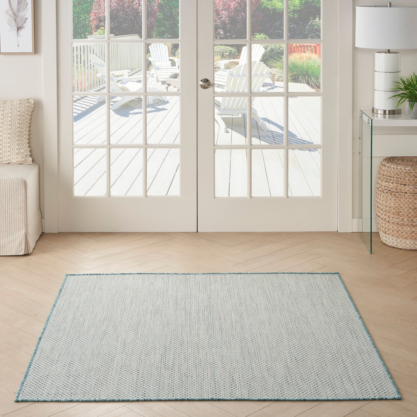 Light gray square rug with a blue border on a wood floor in a bright living room by French doors.