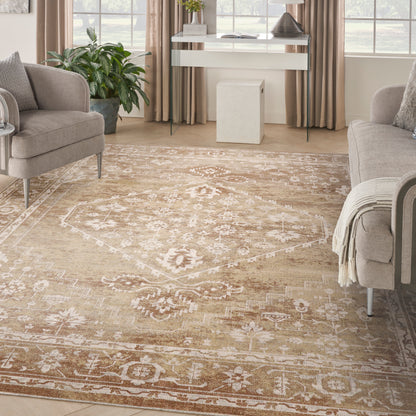 Beige ornate area rug with ivory floral and geometric pattern in a bright living room with taupe sofas and a green plant.