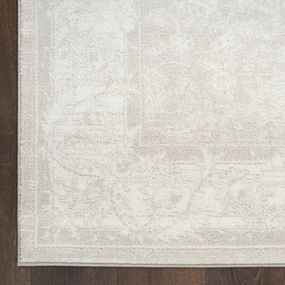 Beige patterned area rug with subtle border and floral motifs, placed on dark wood flooring.