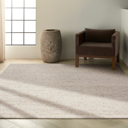 Neutral living room with textured beige rug, brown velvet armchair, & a tall rough stone vase beside a grid-window.