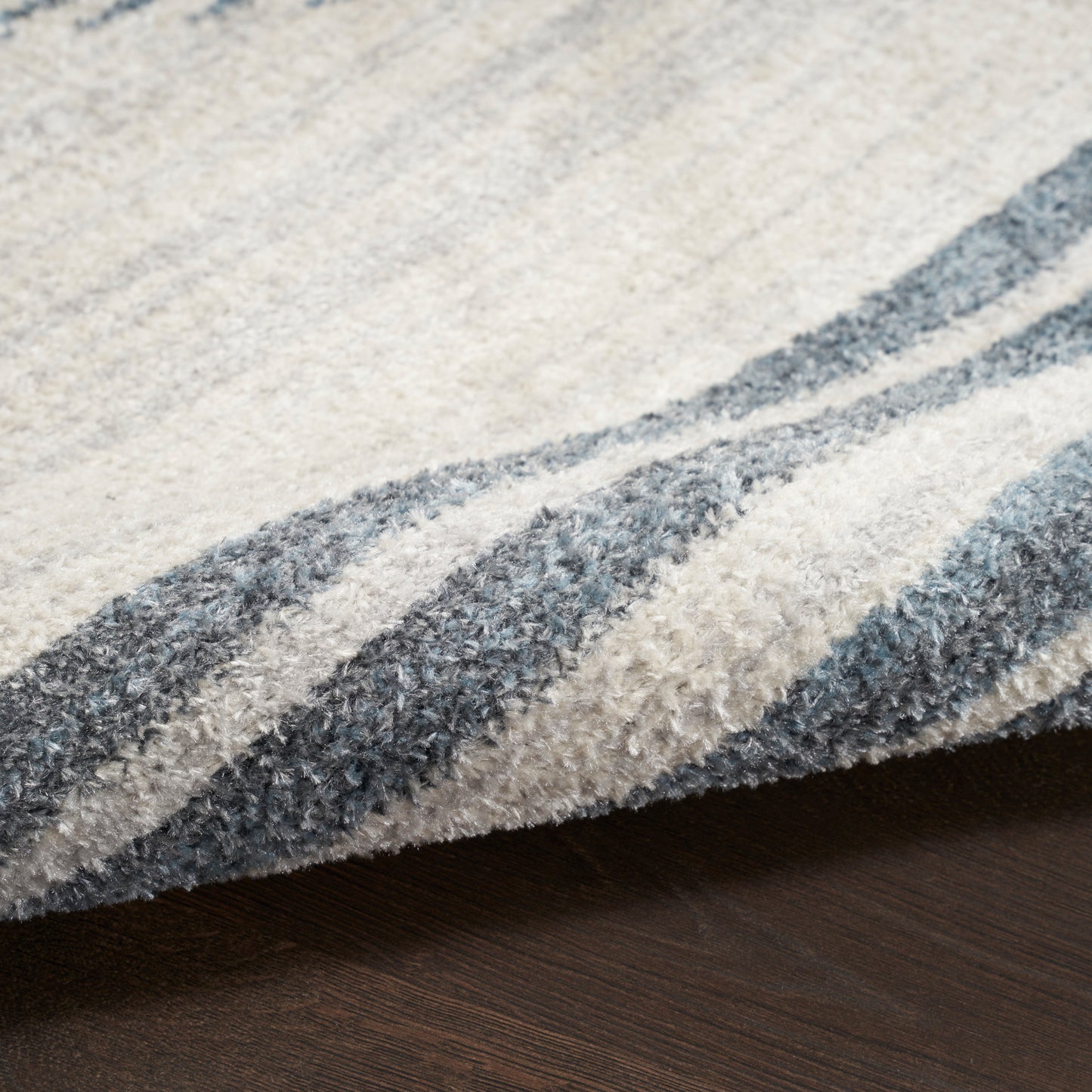 Close-up of a plush beige and gray striped rug with a folded edge on dark wood floor.