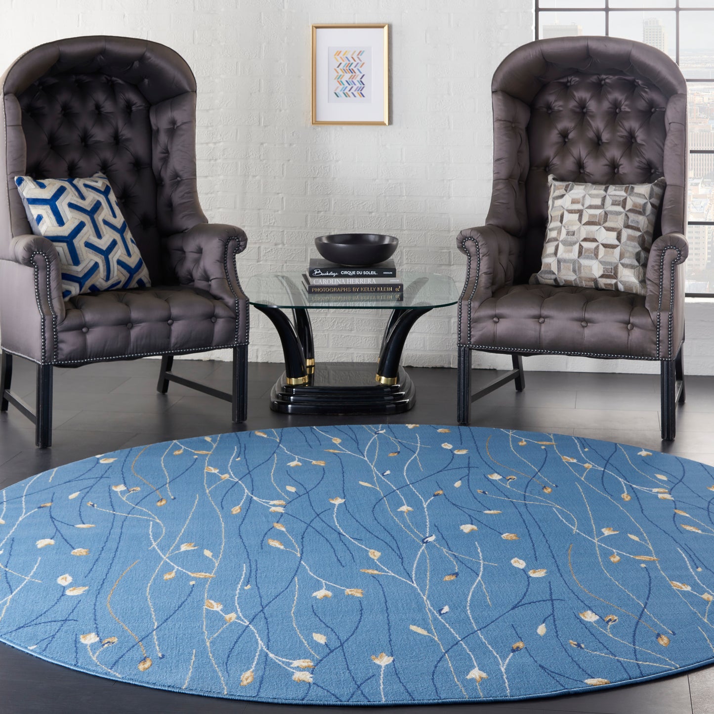 Blue patterned round rug (8' diameter) under two dark brown tufted leather armchairs with nailhead trim and a glass round coffee table.