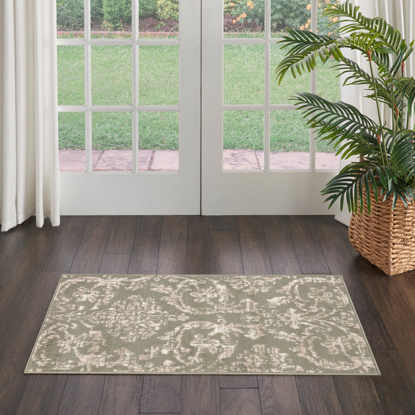 Beige patterned area rug with subtle floral motif on dark wood floor by French doors; potted palm in wicker planter.