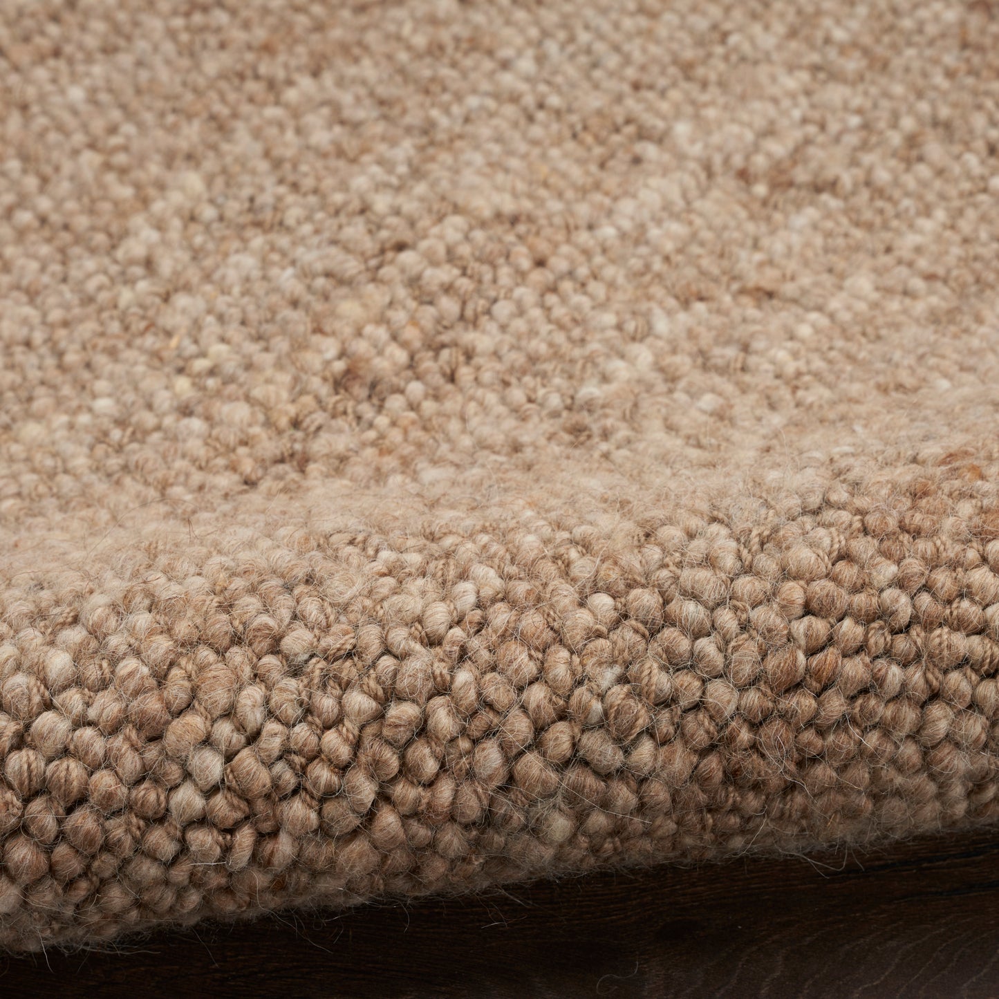 Beige boucle rug close-up with soft, nubby texture and folded edge on dark wood floor.
