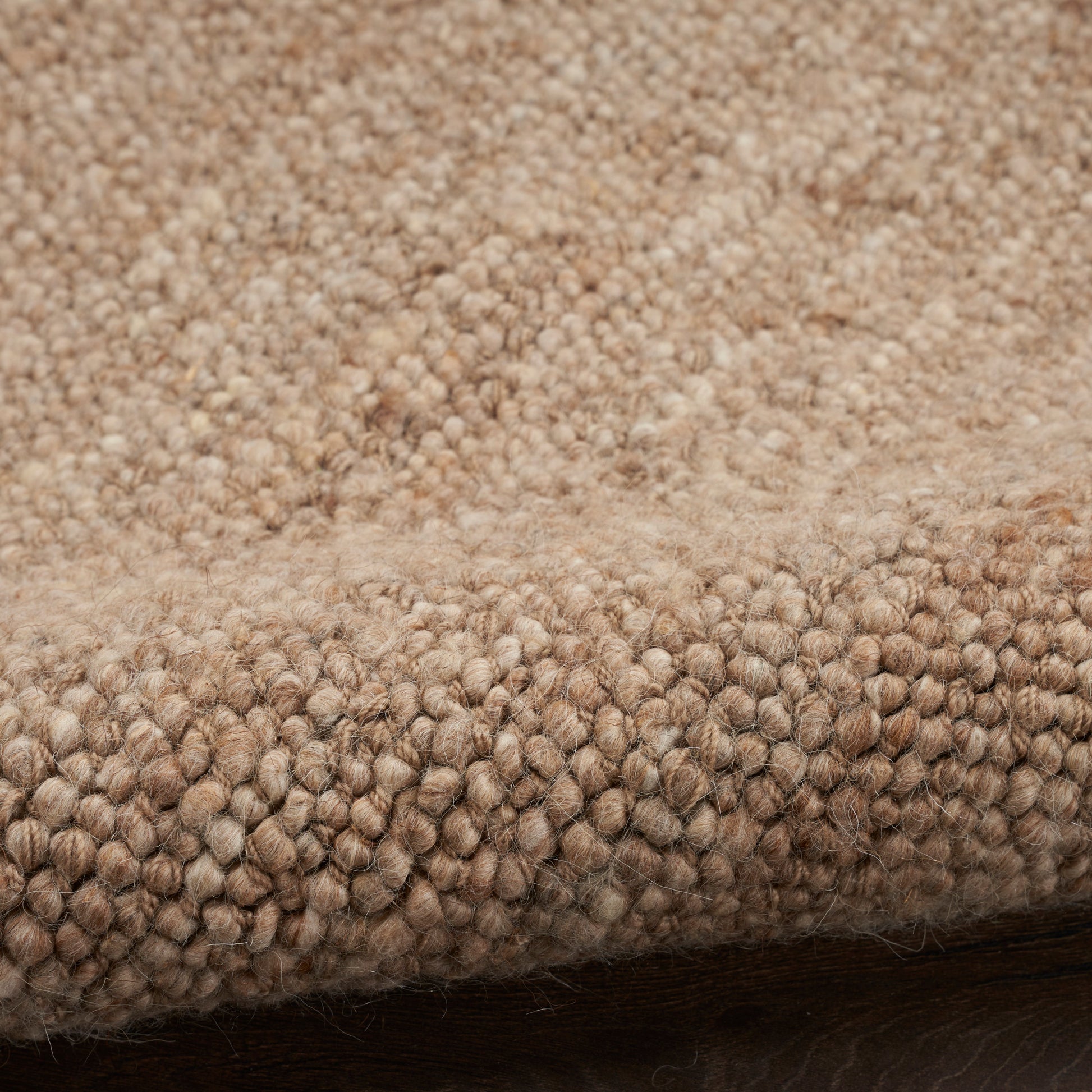 Beige boucle rug close-up with soft, nubby texture and folded edge on dark wood floor.