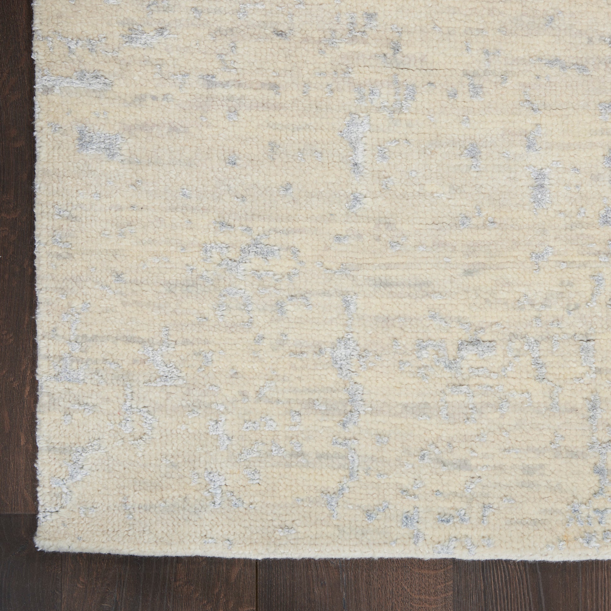 Cream-beige area rug with soft gray abstract pattern and textured pile on dark wood floor.