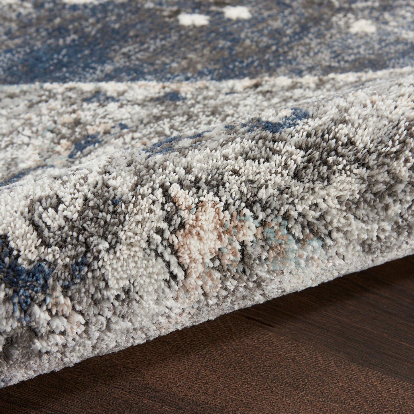Close-up of a plush shag rug with blue, gray, and ivory tones and a thick, dense pile on a dark wood floor.
