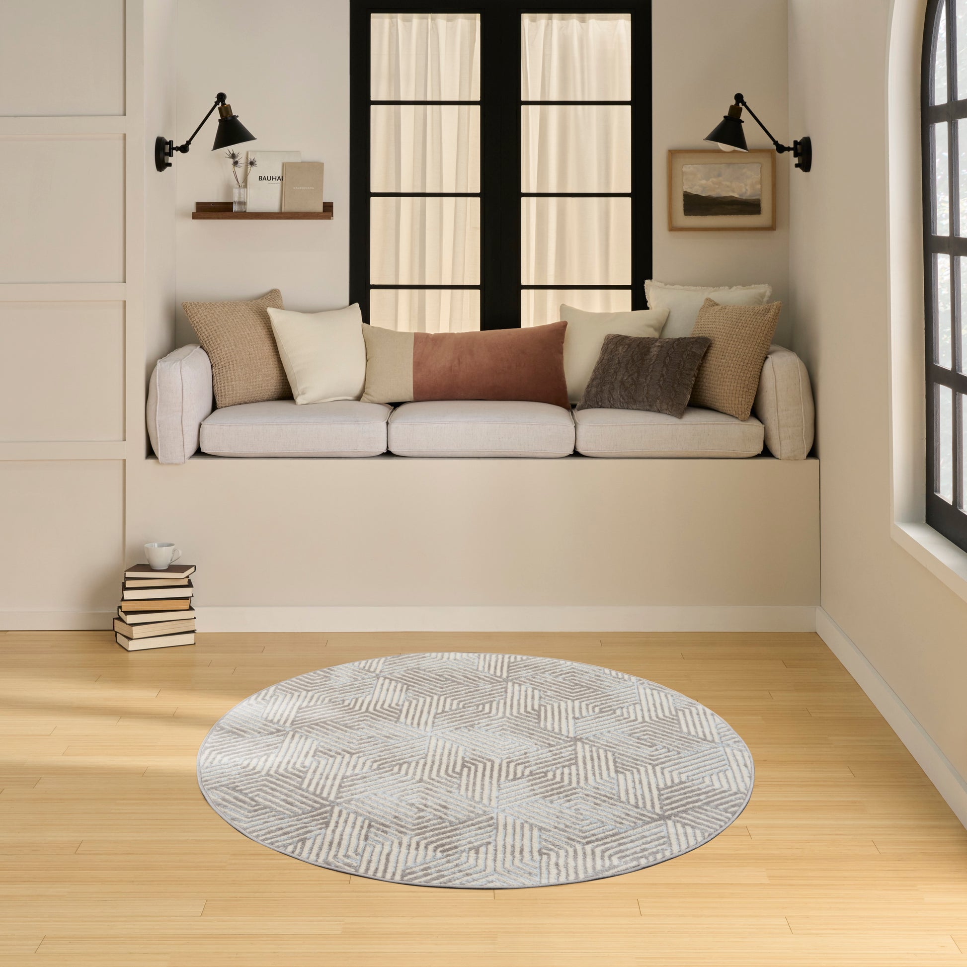 Cozy built-in window-seat with neutral cushions, pillows, black wall lamps, and round gray rug on light wood floor.
