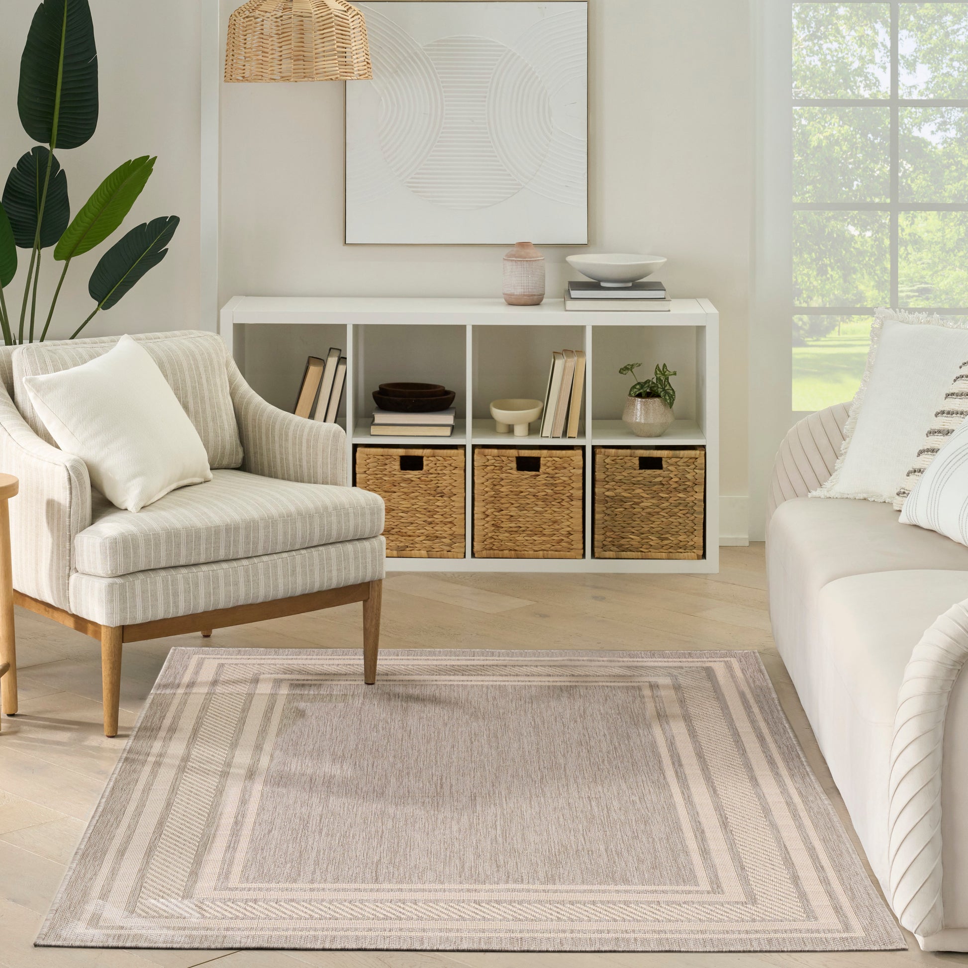 Bright neutral living room with white cubby shelves, wicker baskets, beige armchair, pale sofa, woven lamp, rug.