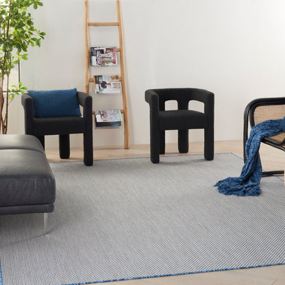 Modern living room with black sculptural armchairs, gray rug, wooden ladder shelf, leafy plant, and a blue throw blanket.