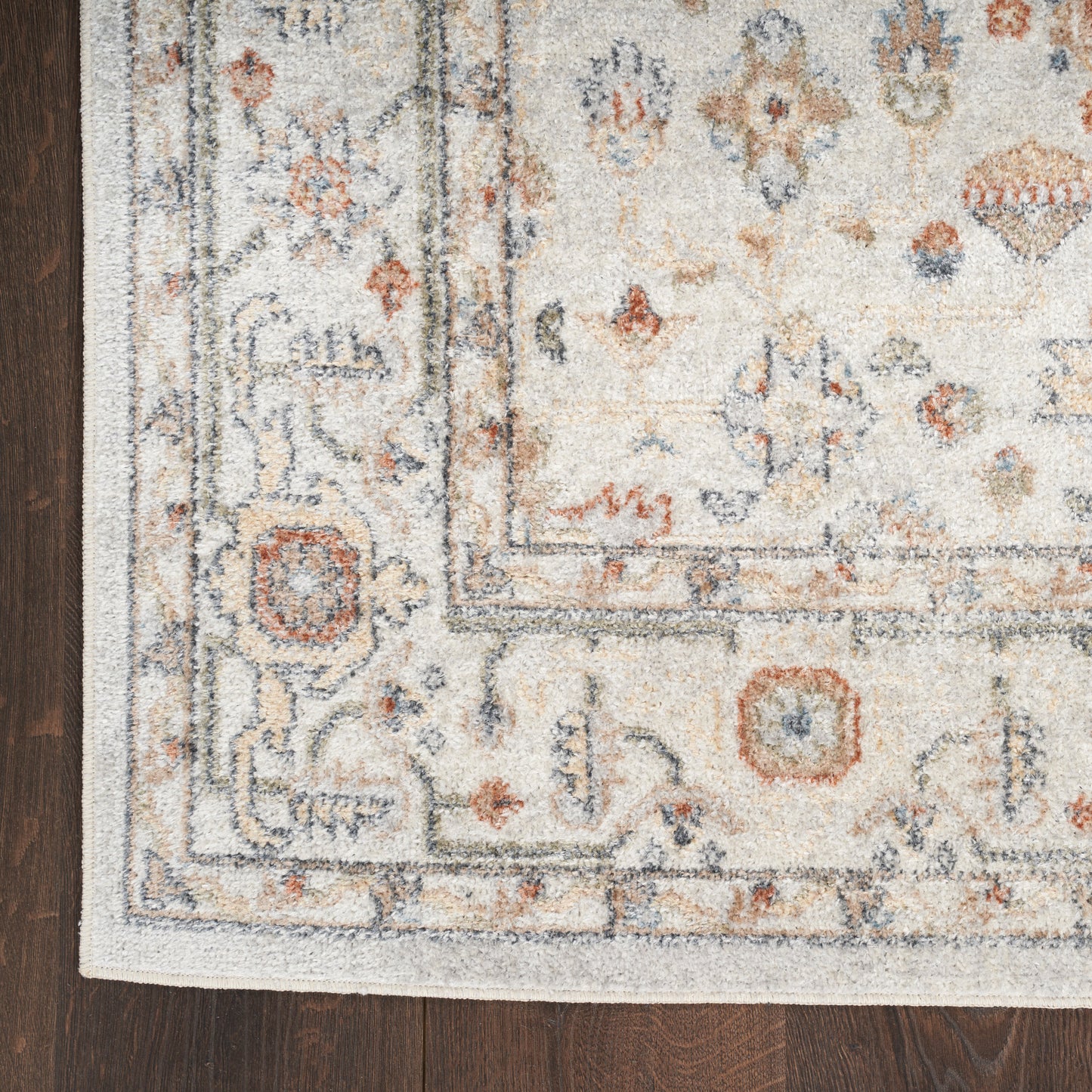 Cream oriental rug with blue and rust accents, geometric border, fringed edges on dark wood floor.