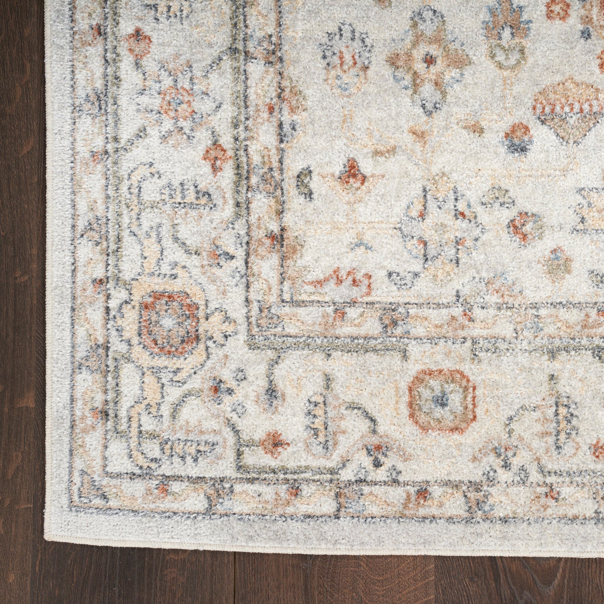 Cream oriental rug with blue and rust accents, geometric border, fringed edges on dark wood floor.