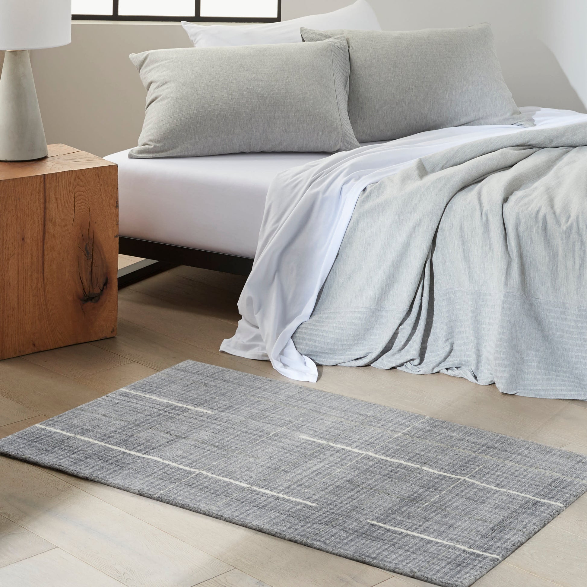 Modern bedroom with a light gray duvet, matching pillows, a draped blanket, and a gray striped rug.