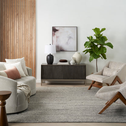 Modern living room with dark wood sideboard, abstract art, vases, large green plant, beige lounge chairs & gray rug.