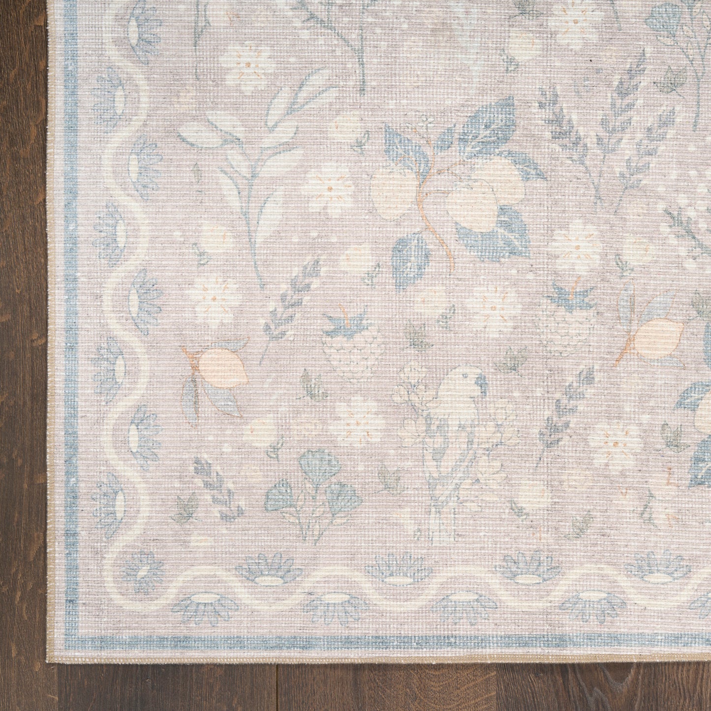 Pastel floral area rug with soft beige background, blue flowers, and a pale blue border on dark wood floor.