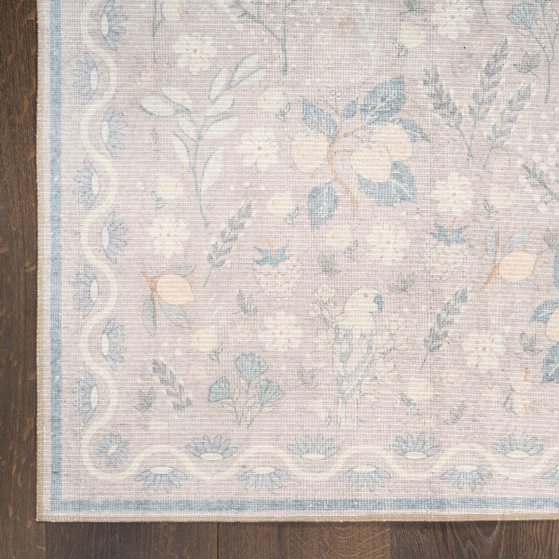 Pastel floral area rug with soft beige background, blue flowers, and a pale blue border on dark wood floor.