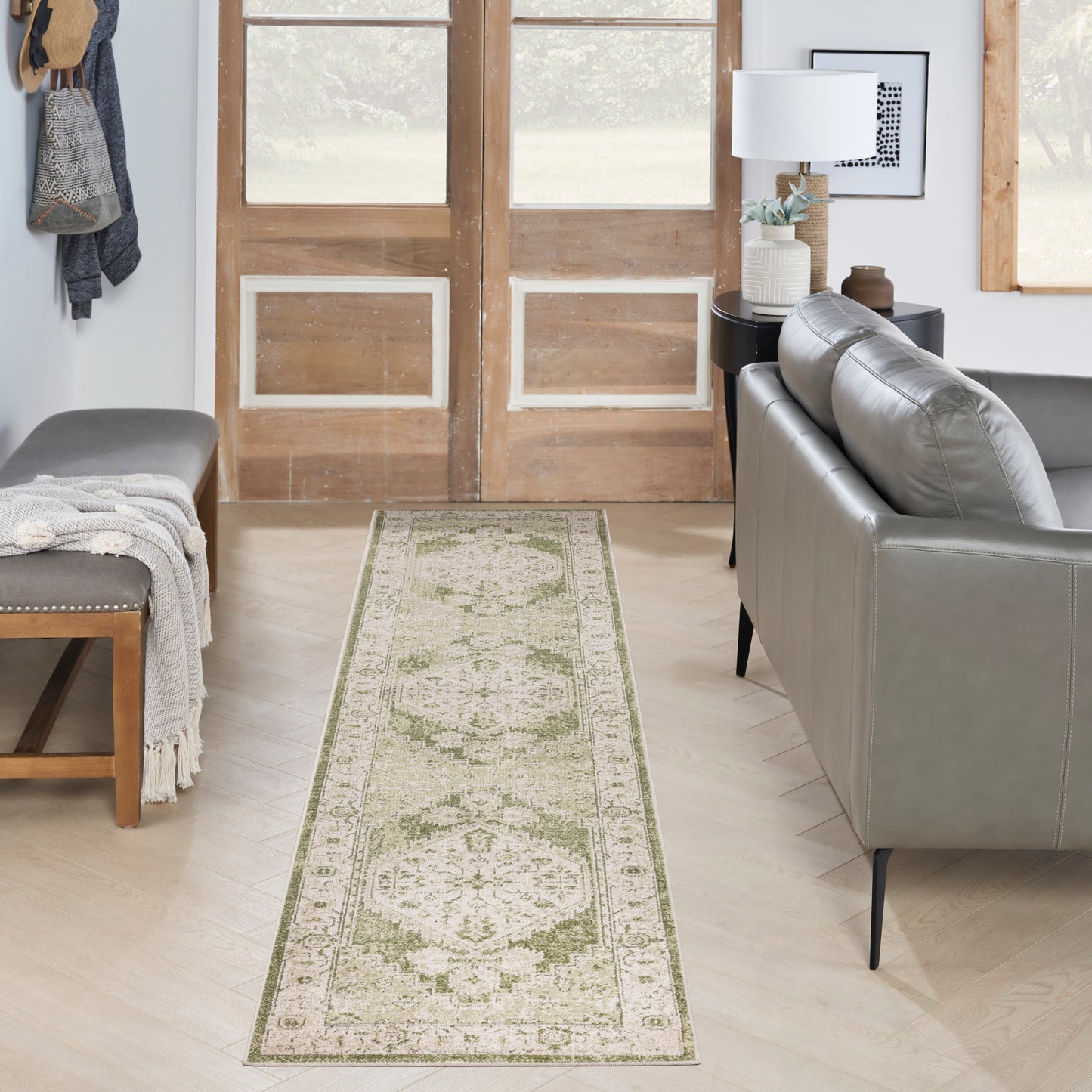Ivory and sage green Persian-style runner rug in a bright living room with a gray sofa, wooden doors, bench, and throw.