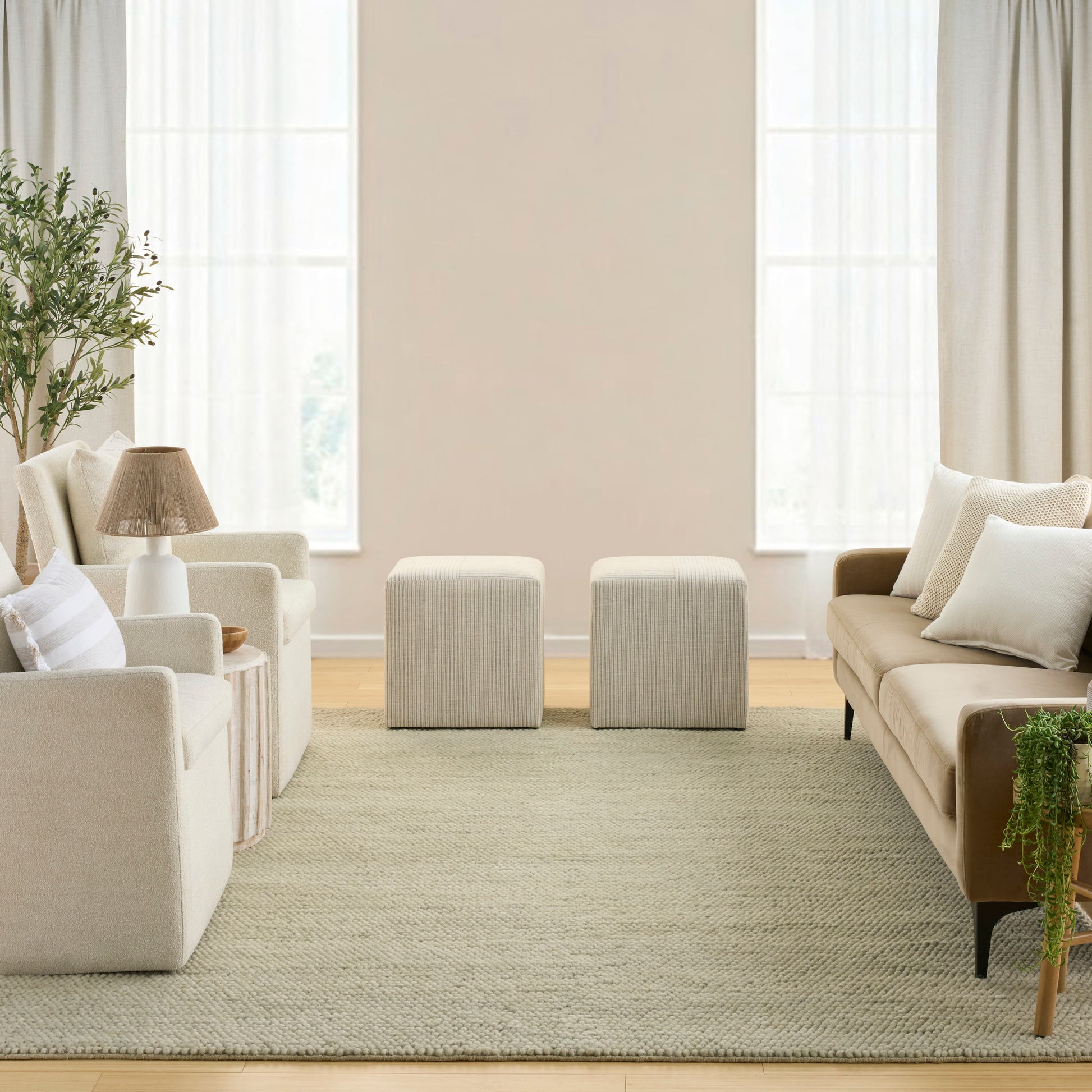 Neutral living room with cream fabric sofa and armchairs, two square ottomans, beige rug, and greenery.