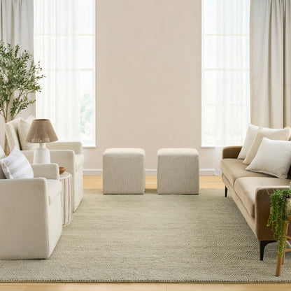 Neutral living room with cream fabric sofa and armchairs, two square ottomans, beige rug, and greenery.