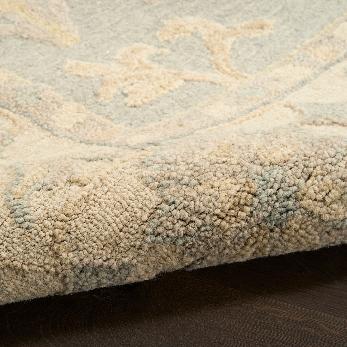 Beige and ivory shag rug with pale blue floral pattern; thick tufted pile, edge resting on dark wood floor.