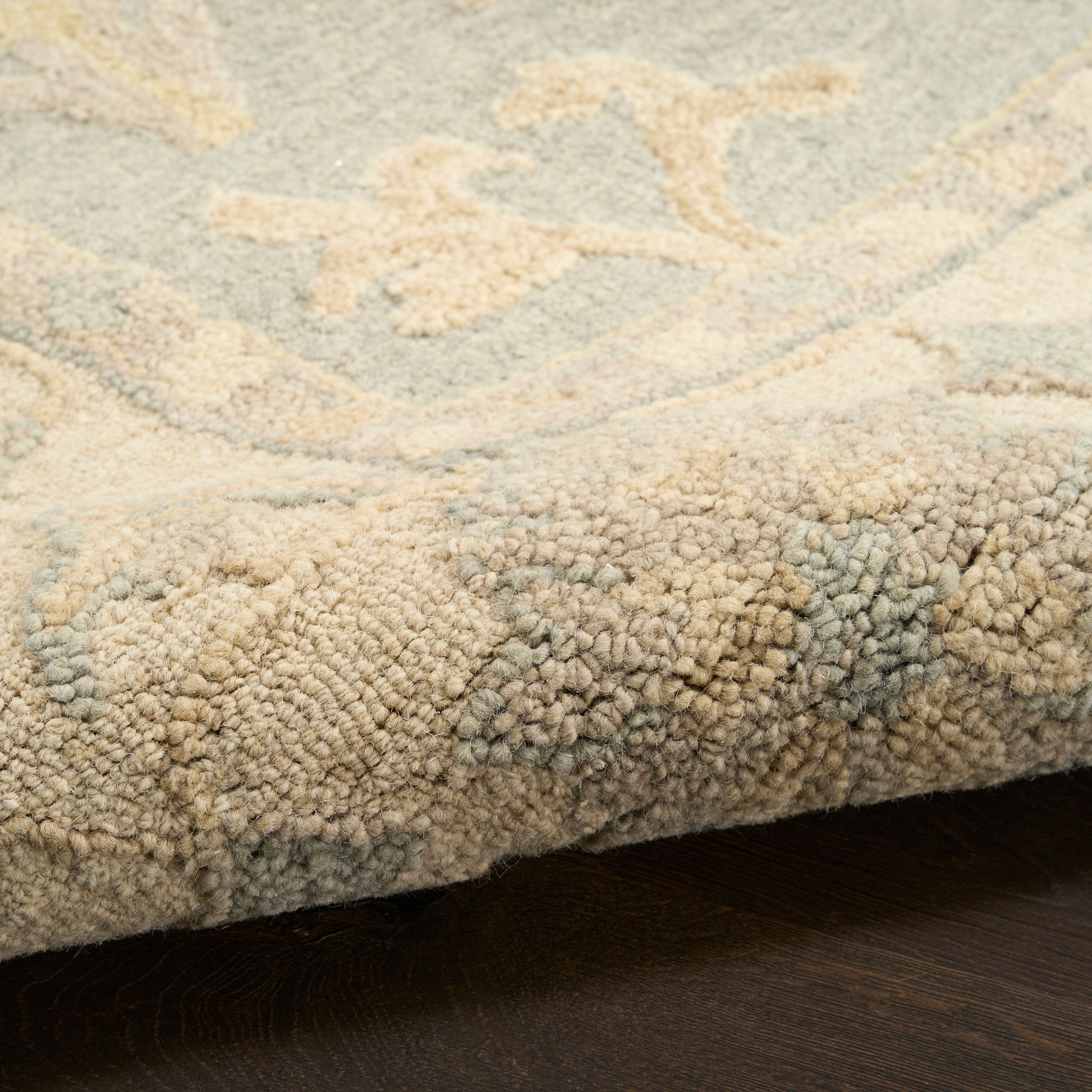 Beige and ivory shag rug with pale blue floral pattern; thick tufted pile, edge resting on dark wood floor.