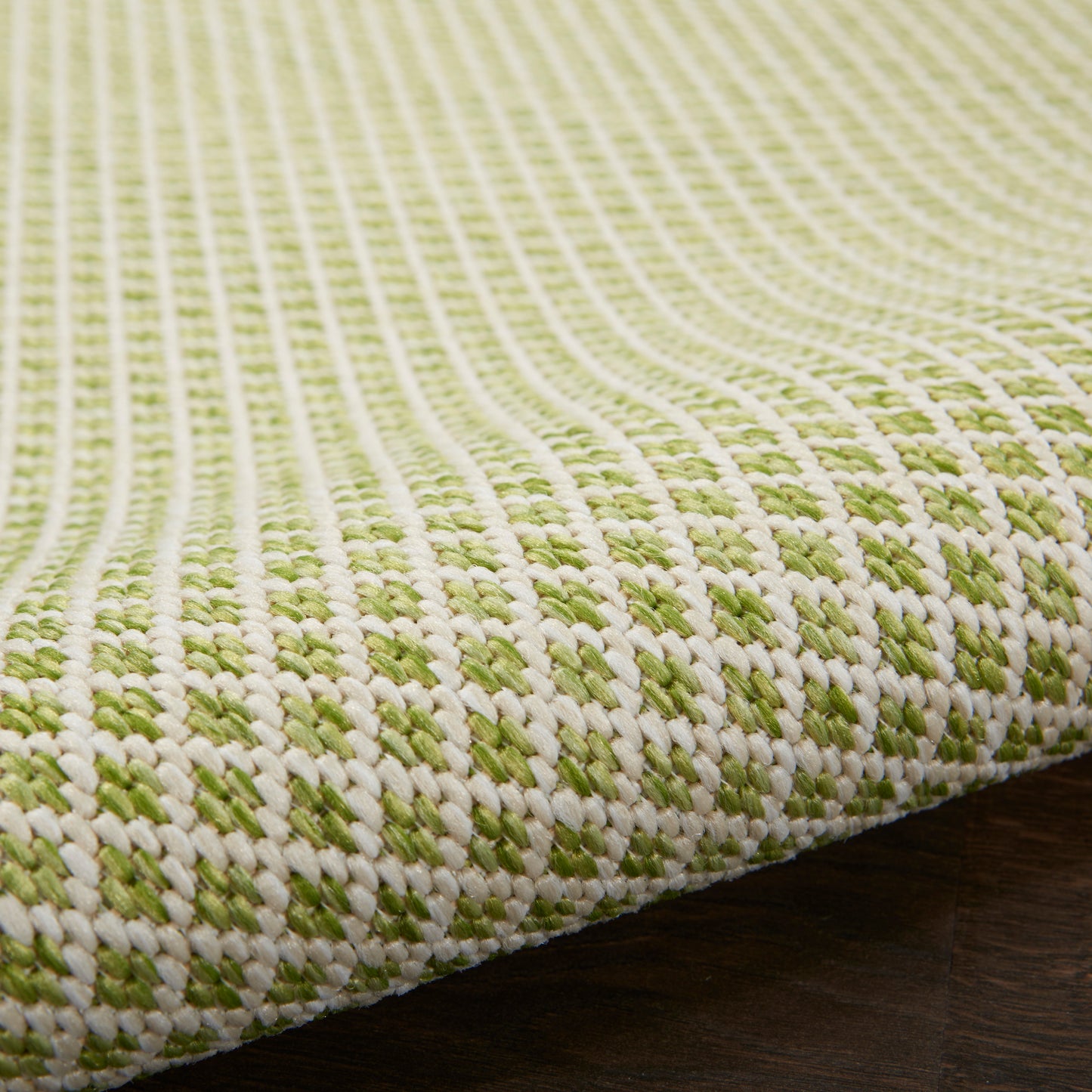 Close-up of a green and ivory woven rug with a chunky textured checker pattern and finished edge.