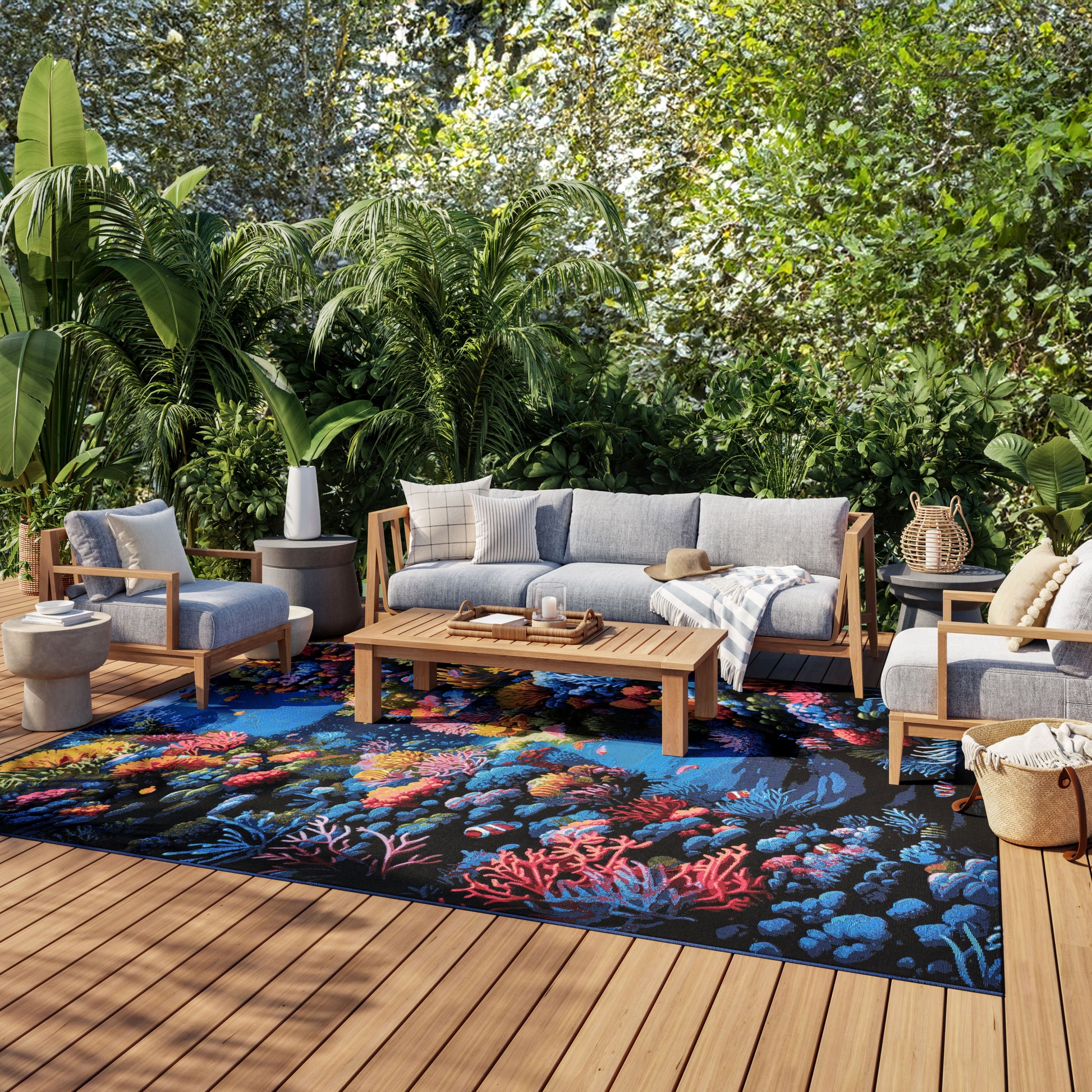 Outdoor lounge with light gray cushioned wooden sofa and chairs, vibrant coral-pattern rug, coffee table, and lush tropical greenery.