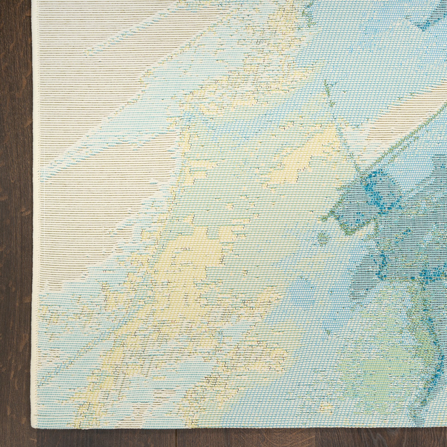 Rectangular woven rug with pastel map design in beige, blue & teal; coastal lands & sea on a dark wood floor.