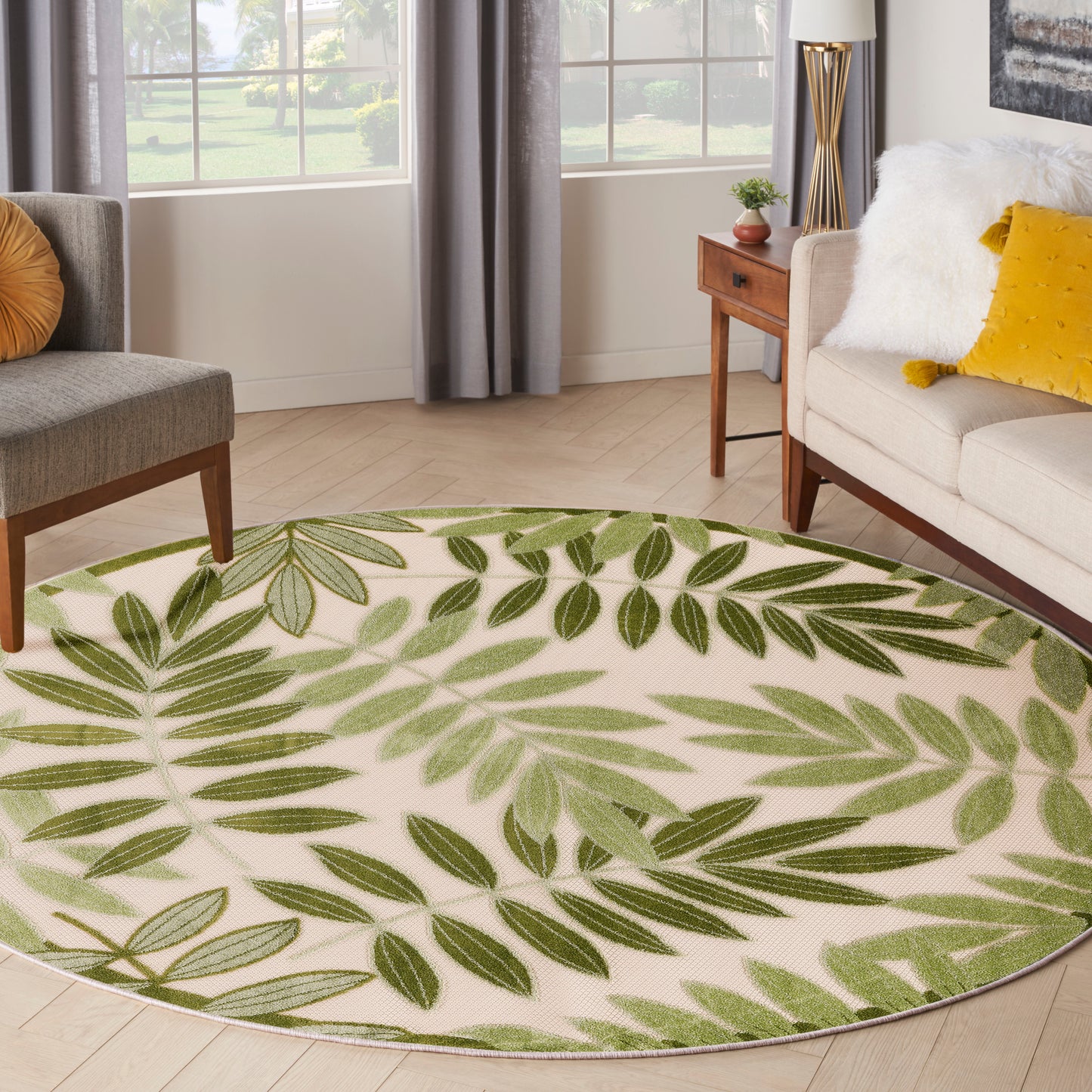 Round beige area rug with green fern leaf pattern, in a modern living room with neutral furniture and mustard pillows.