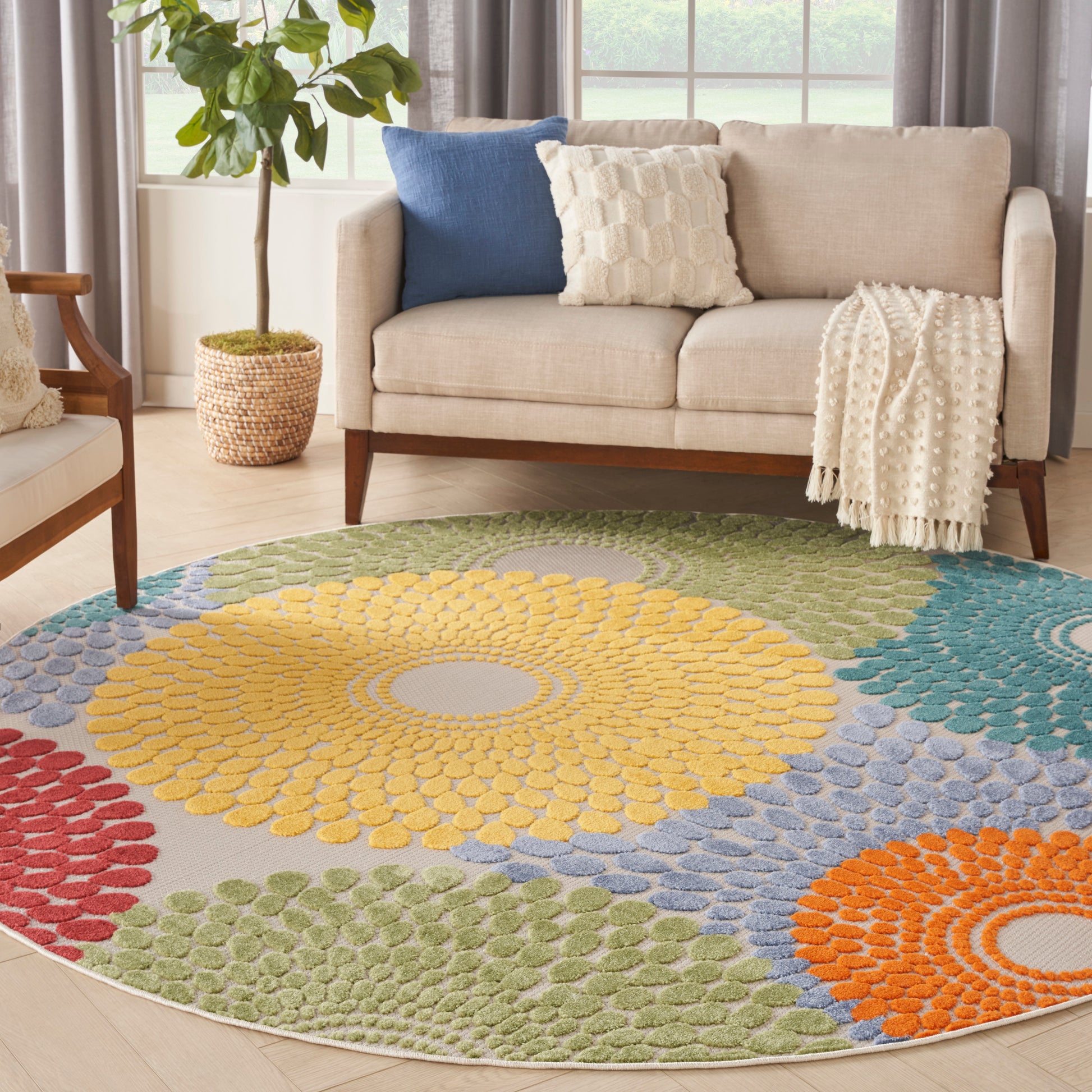 Round tufted rug with multicolor sunburst petals: yellow center, greens, blues, oranges, reds, in a living room.