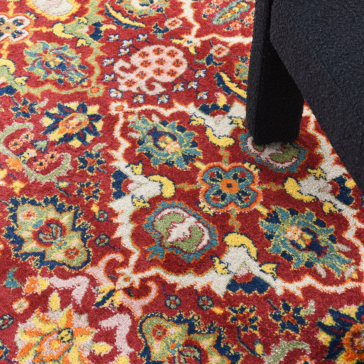 Colorful oriental rug with red base and vivid floral motifs in blue, yellow, green, and white; dark navy chair leg on edge.