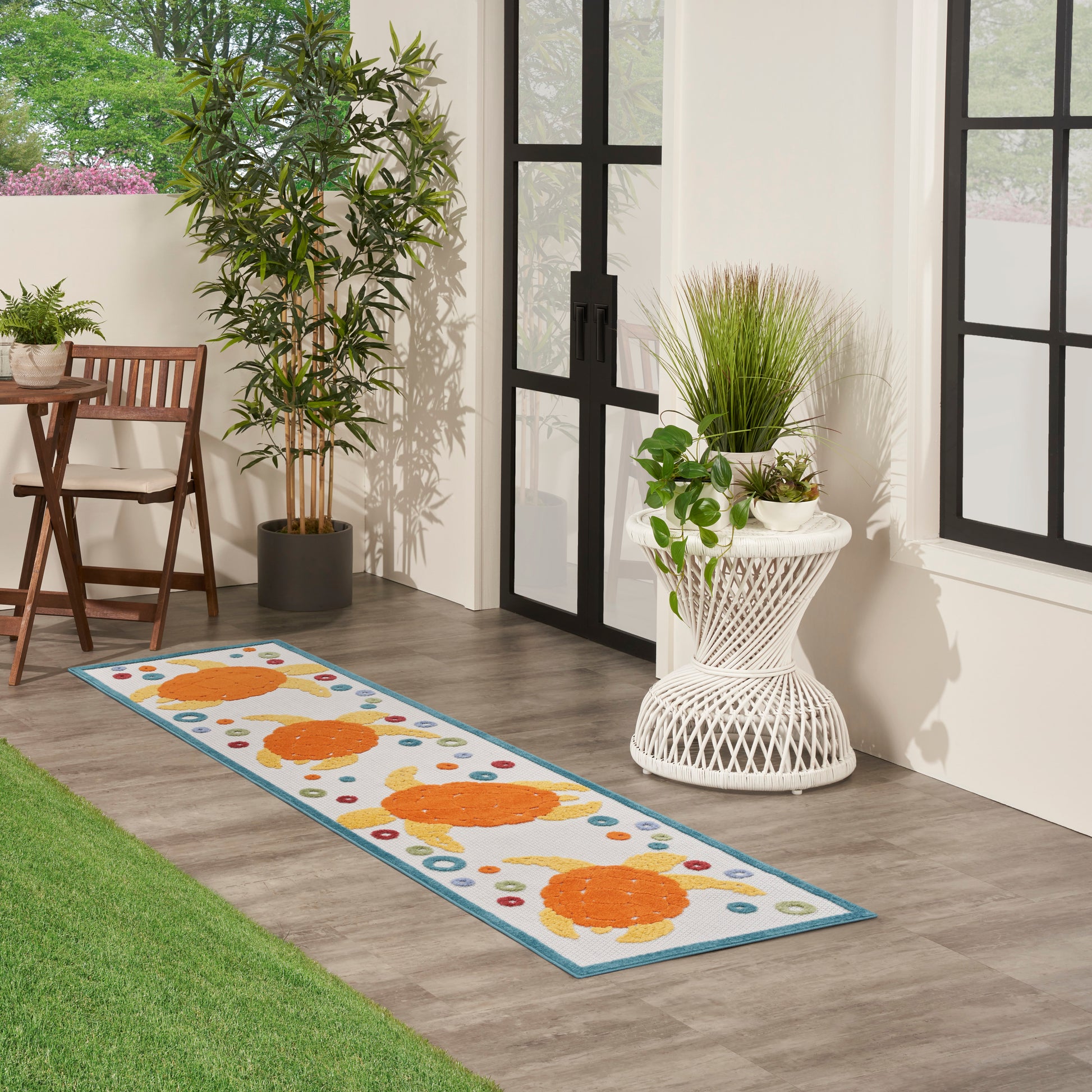 Long blue-bordered runner rug with orange fish motifs in a bright patio entryway with potted plants and wicker furniture.