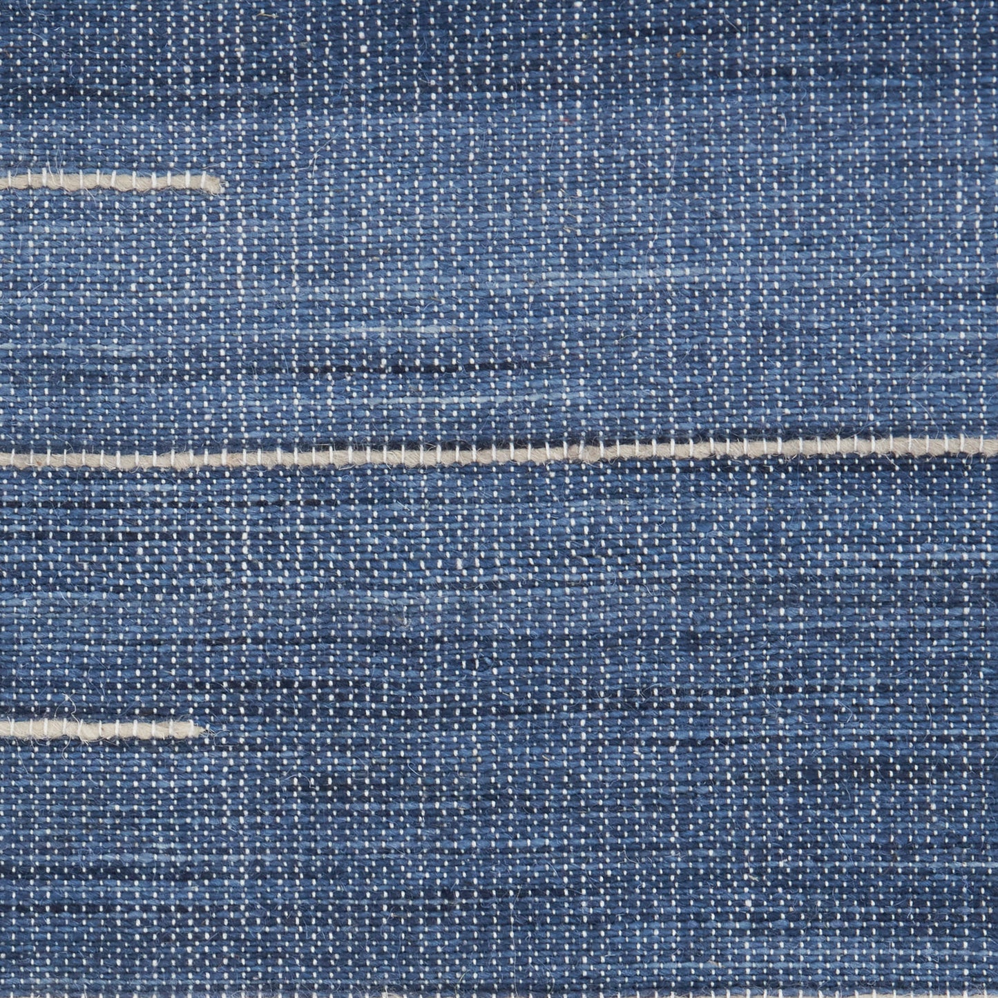 Close-up of blue textured rug fabric with two beige seam lines in a woven texture.