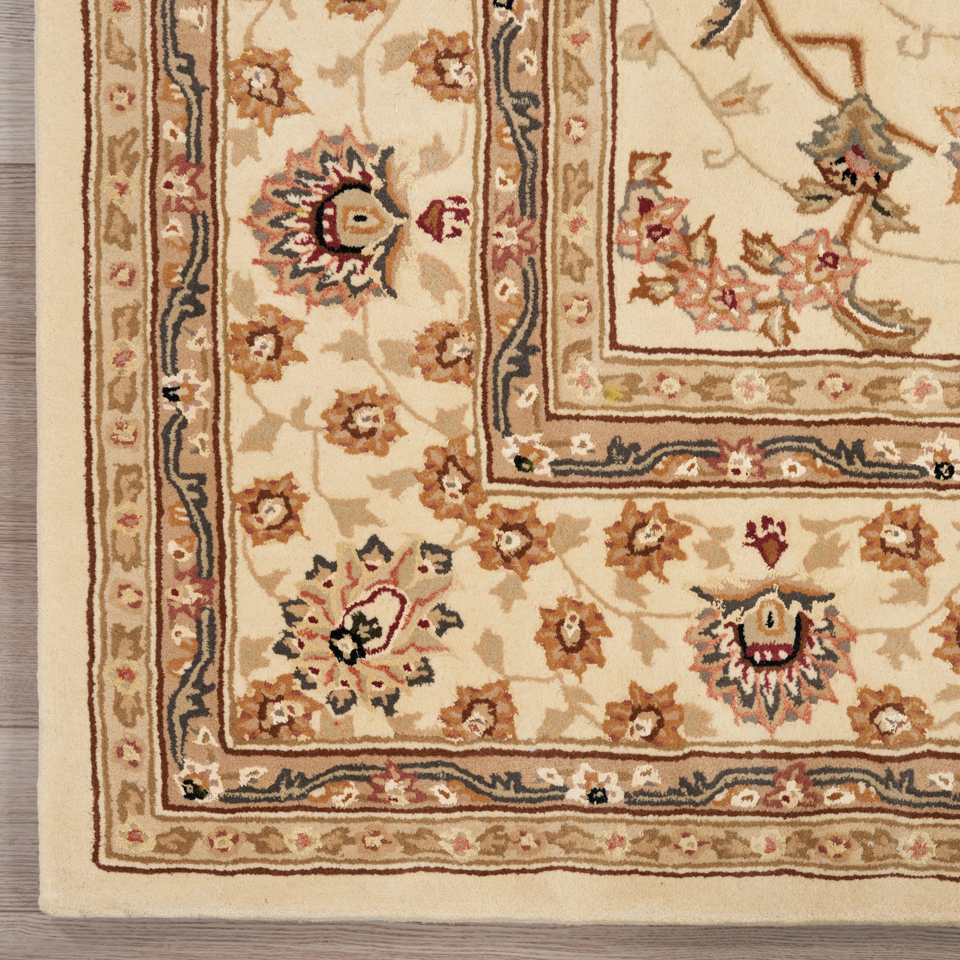 Beige Persian-style rug close-up with layered cream, gold and navy borders and red-blue floral motifs.
