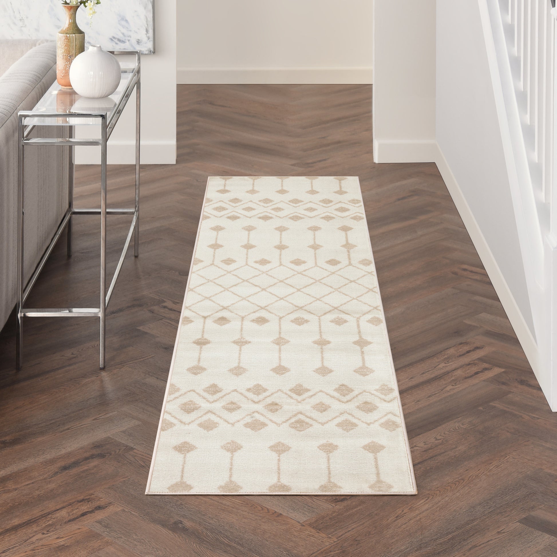 Cream hallway runner rug with taupe geometric motifs on dark wood floor; modern entryway.