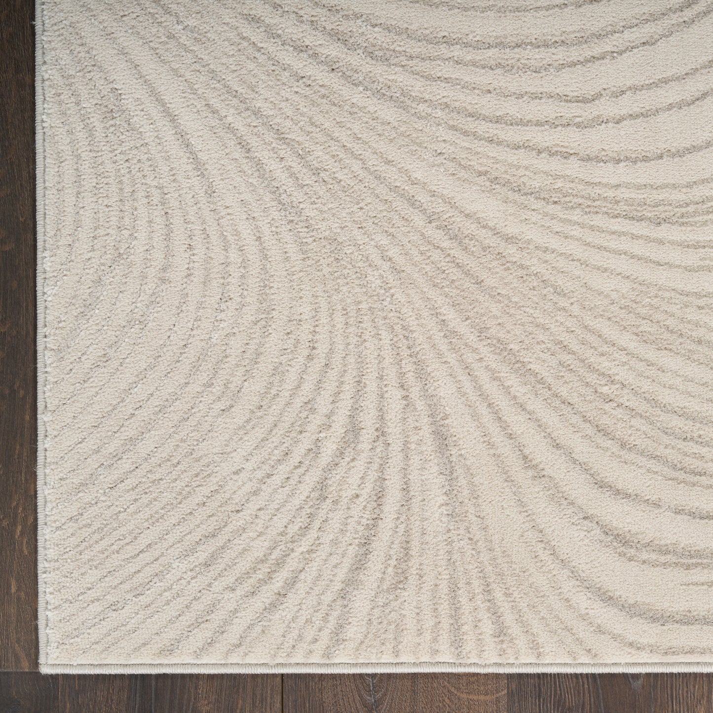 Beige rectangular rug with subtle curved ripple lines and a dark left edge on a dark wood floor.