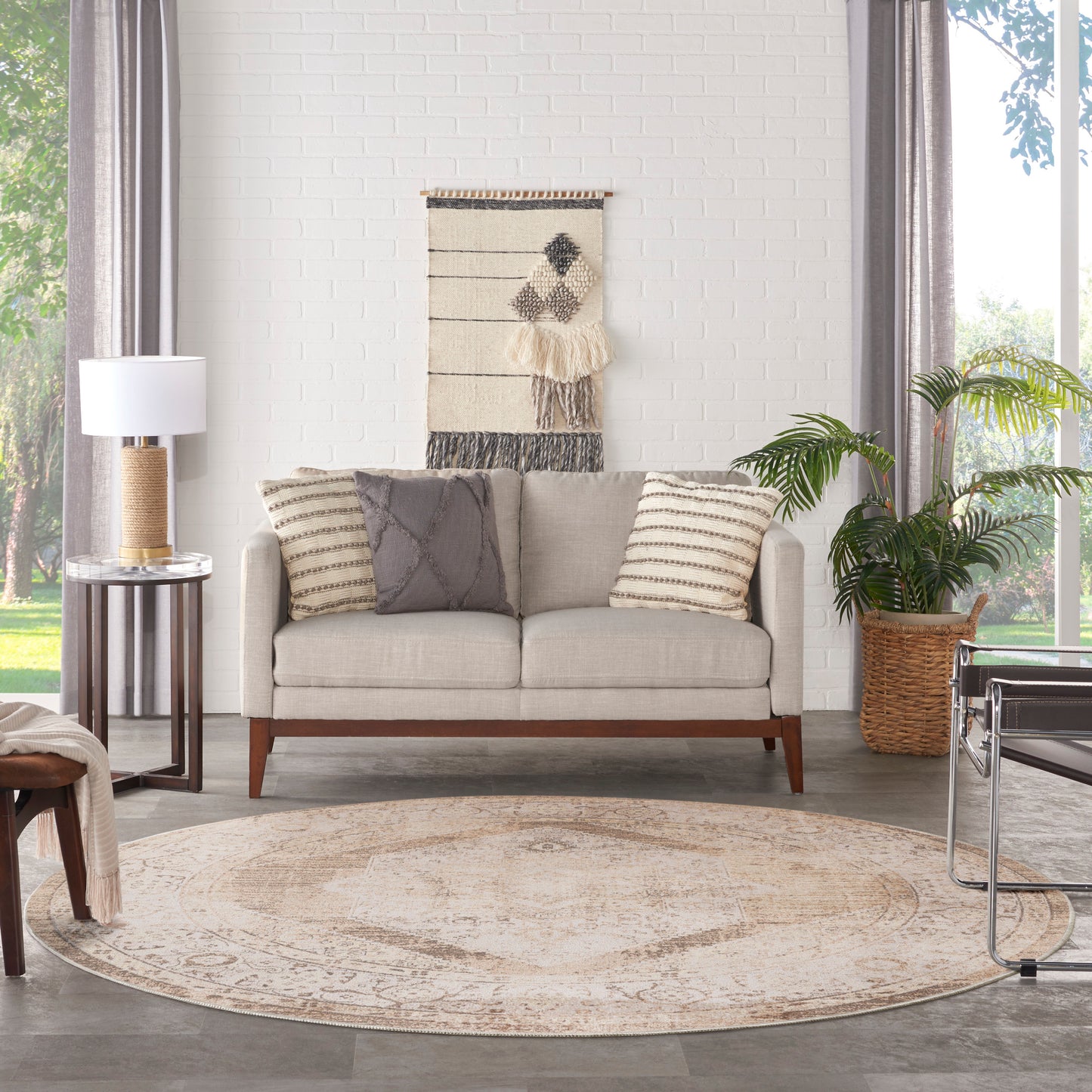 Beige fabric sofa with striped and diamond pillows, round beige rug, boho wall hanging, potted plant in a woven basket.