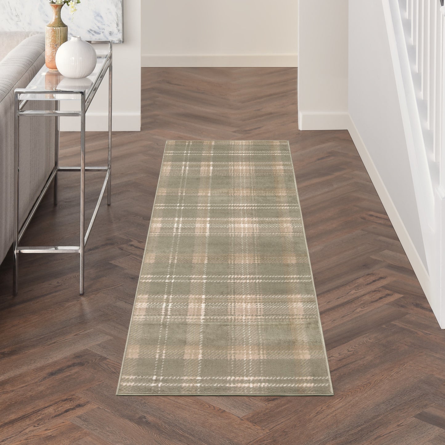 Olive-green plaid hallway runner rug on herringbone wood floor beside a chrome-framed glass console with vases.