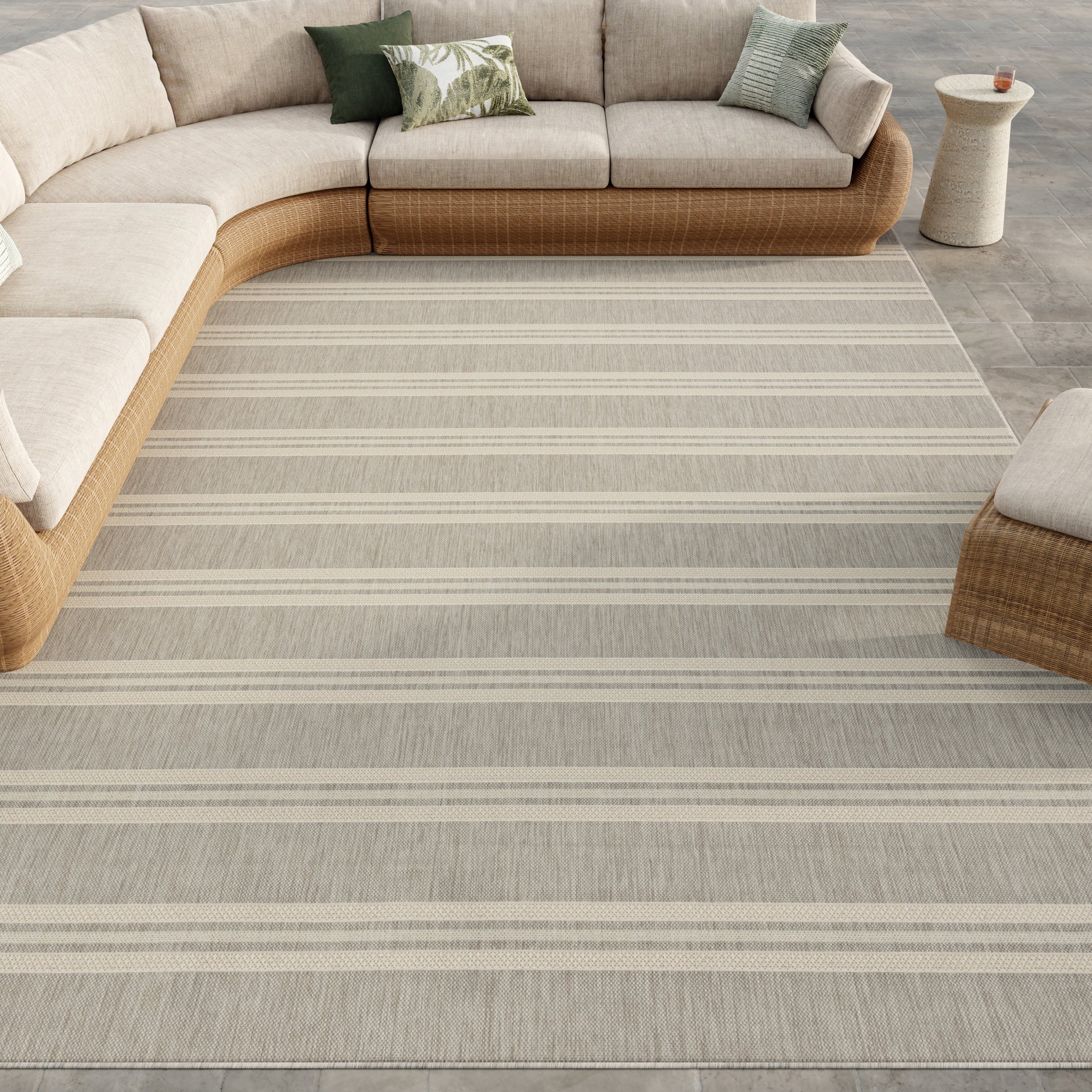 Beige curved wicker sectional with cream cushions & a small round side table, on a striped beige outdoor rug.