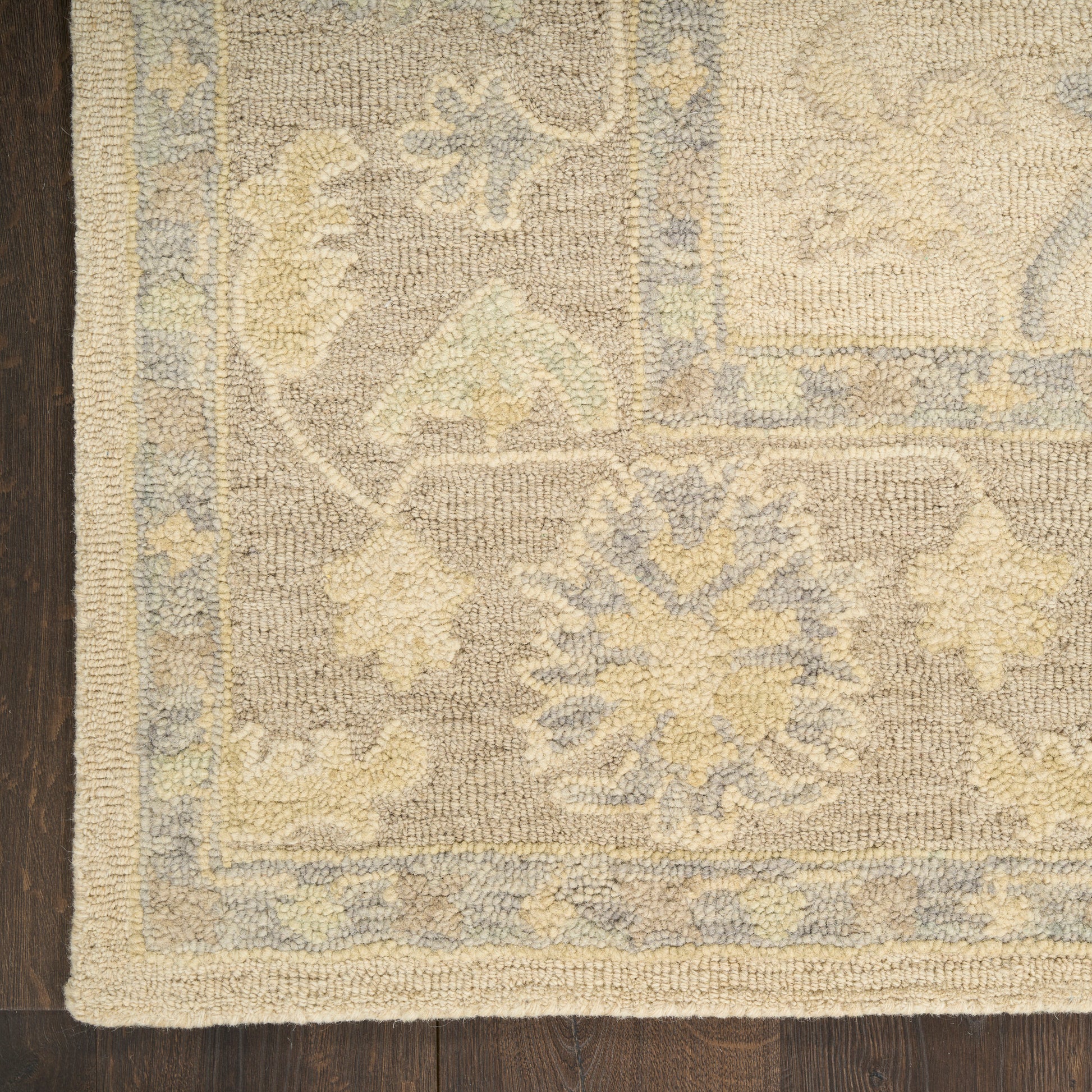 Rectangular woven rug with muted gray-beige field, pale yellow and light blue floral medallions and a blue border on dark wood floor.