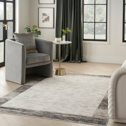 Gray upholstered armchair with cushion, beside a round marble-top brass side table on a neutral patterned rug in a modern living room.
