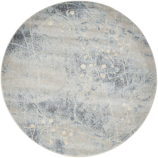 Round blue-gray rug with soft cloud-like texture and white botanical branch pattern.