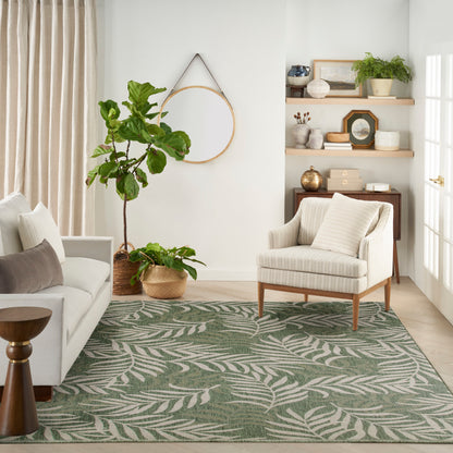 Bright outdoor space featuring a palm-leaf patterned green rug, outdoor seating and tall plants.