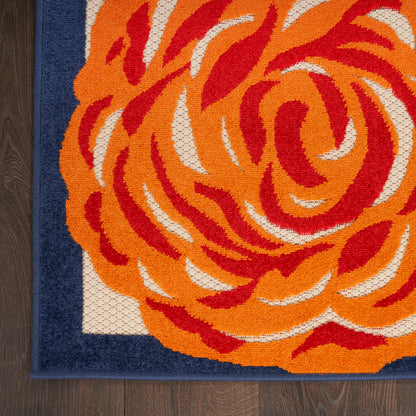 Rectangular woven rug with bold orange red rose motif on white field and navy border, laid on dark wood floor.
